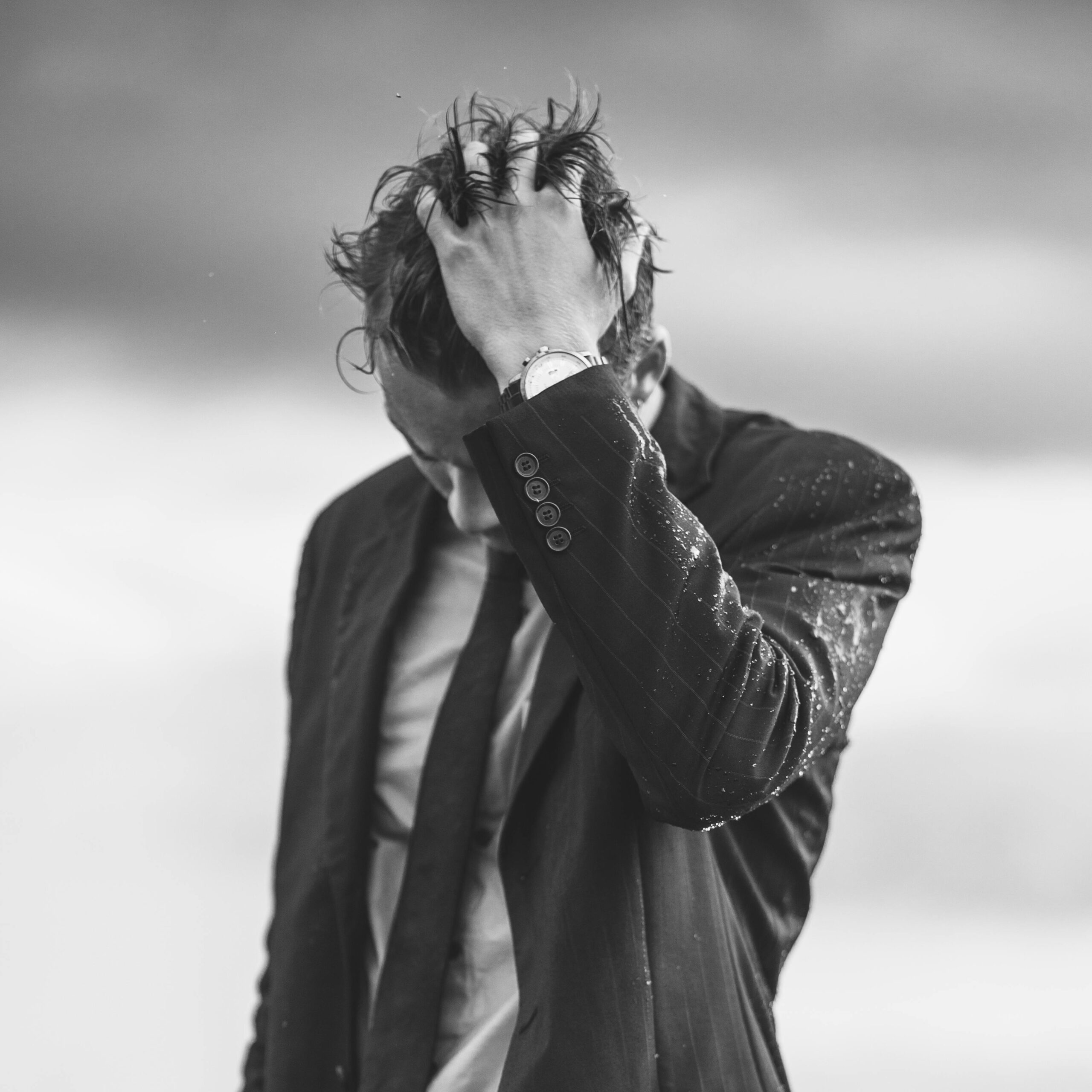 Black and white photo of a man in business attire outdoors, looking down with wet hair.